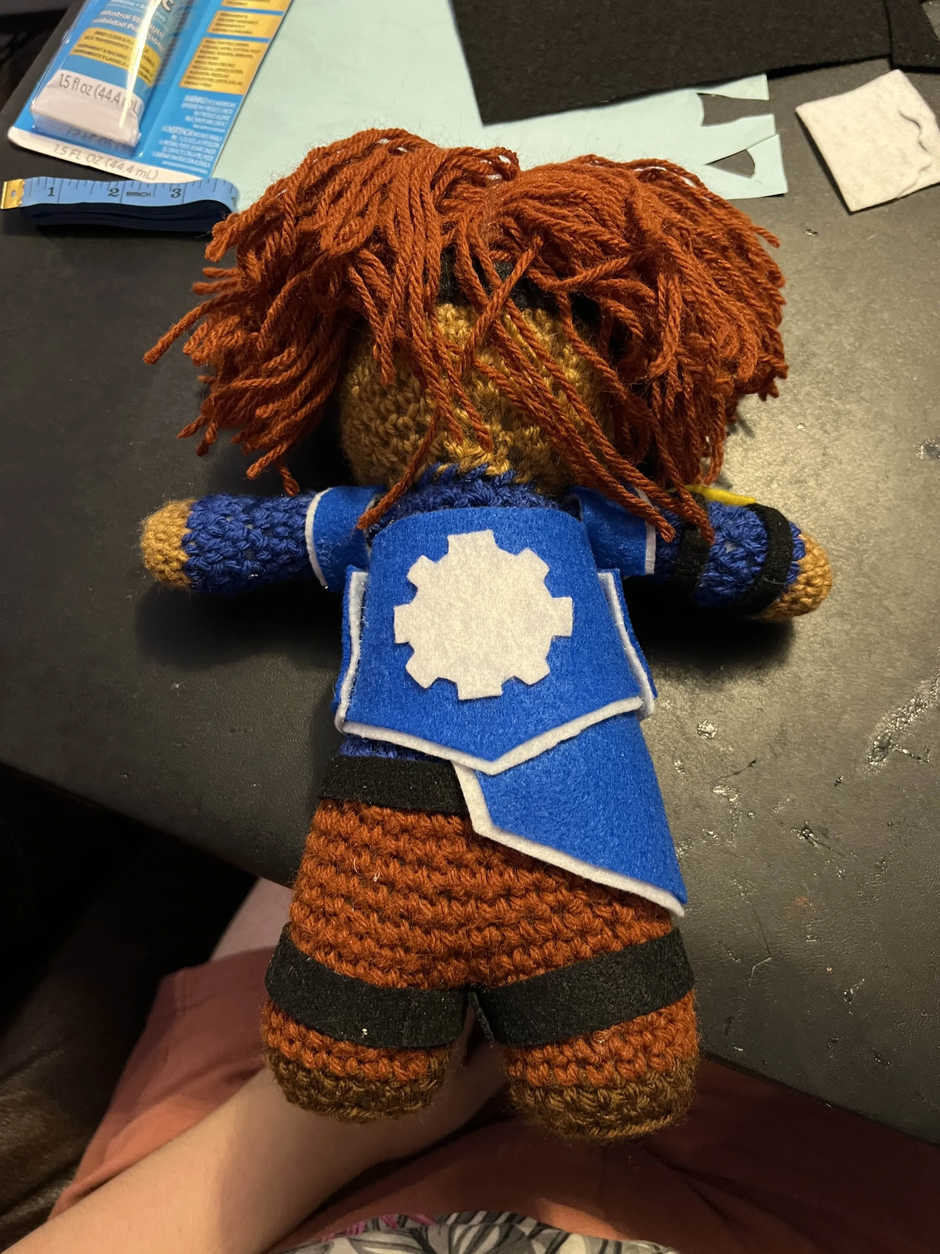 Back of crochet doll showing white gear design on the clothes